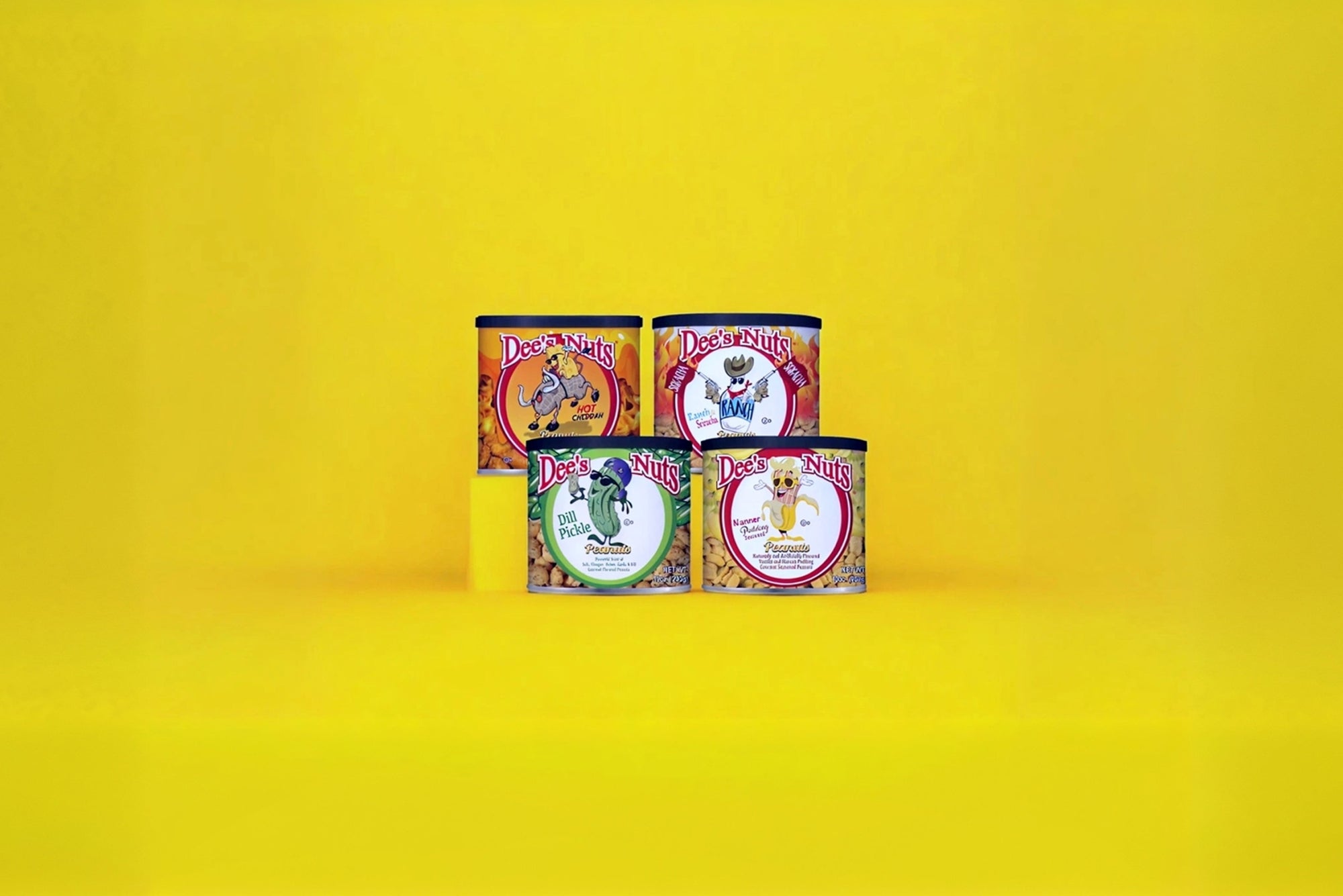 Four colorful cans of Dee's Nuts flavored peanuts stacked against a bright yellow background, featuring flavors like Hot Cheddar, Banana Pudding, Dill Pickle, and Enchilada.