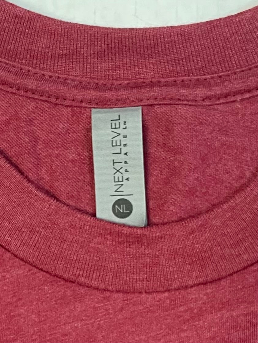 Close-up image of a red t-shirt collar with a visible neck tag that reads “NEXT LEVEL APPAREL” and includes the brand's circular "NL" logo at the bottom of the tag. The fabric appears soft and heathered, indicating a high-quality casual wear garment.