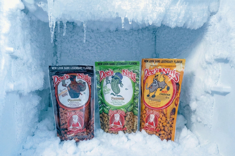 Three packs of Dee’s Nuts flavored peanuts displayed inside a freezer, surrounded by ice and frost, showing different flavors kept frozen for freshness.