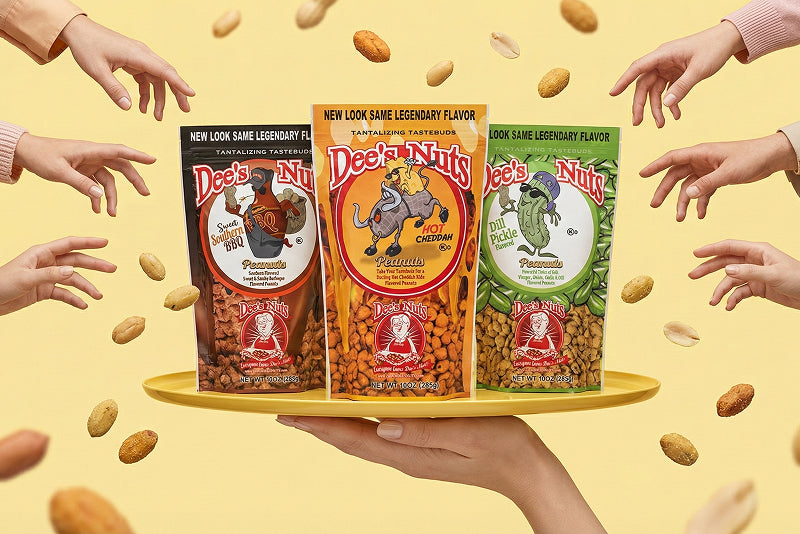 Three packs of Dee’s Nuts flavored peanuts displayed on a tray, with peanuts floating around and multiple hands reaching in against a bright yellow background.