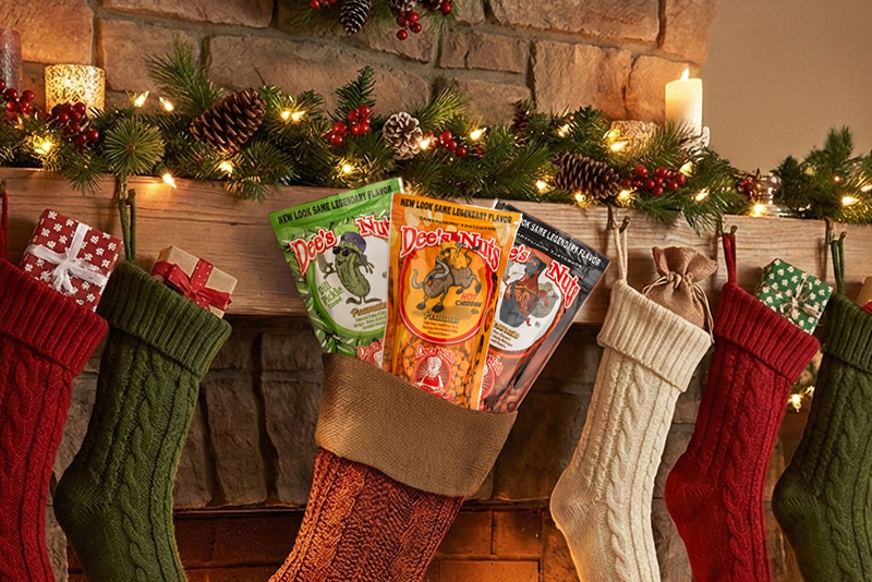 Dee’s Nuts flavored peanut packs arranged inside Christmas stockings hanging on a decorated fireplace mantel for a festive holiday gift display.