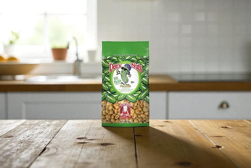 A bag of Dee’s Nuts Dill Pickle flavored peanuts displayed on a wooden kitchen table with a bright, blurred kitchen background